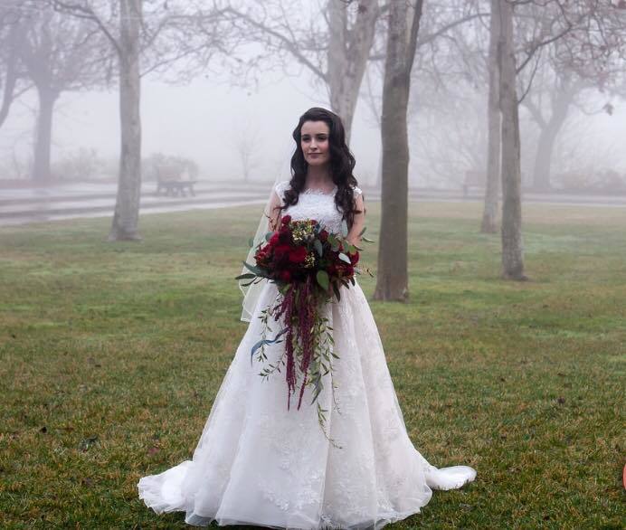 A bride stands in a foggy park, gracefully holding her bouquet, surrounded by a serene and ethereal atmosphere.