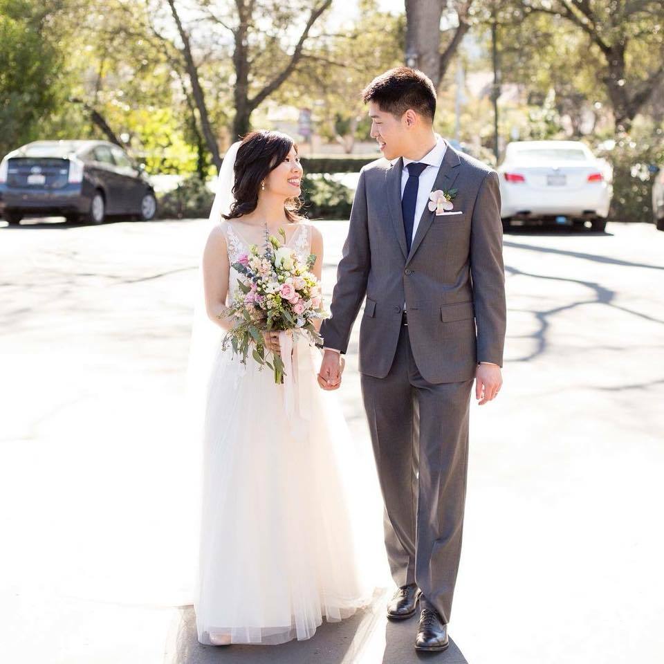 A bride and groom stroll down the street, radiating joy in their wedding attire.